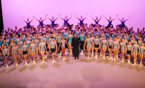 Majesty The Queen Consort Celebrates Elmhurst Ballet School Centenary. Queen Camila stage on stage with a large number of ballet young ballet dancers with pink lighting