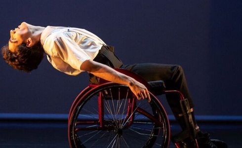 white male in a wheel chair bending backwards on a stage