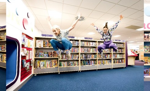 three images of two female dancers jumping and moving in a colourful library 