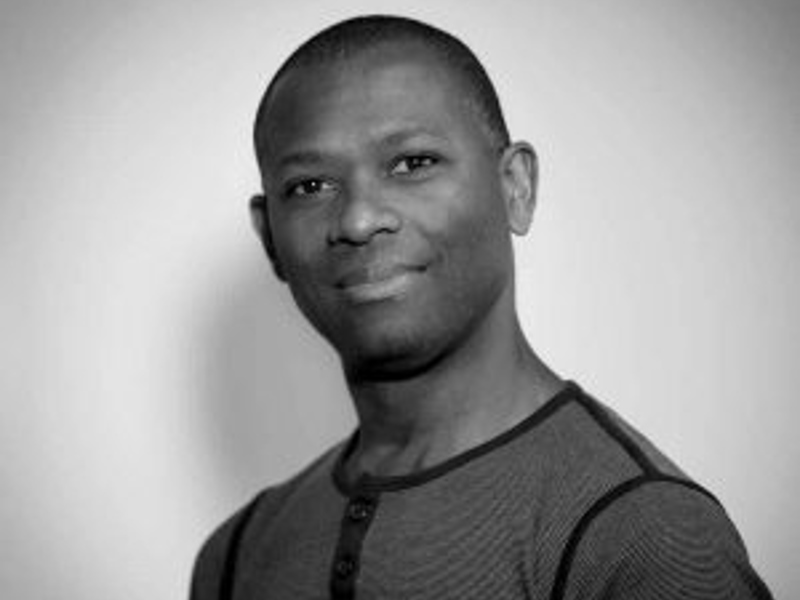 Black and white headshot of Richard Lessey. Global majority male with bald head looking at the camera