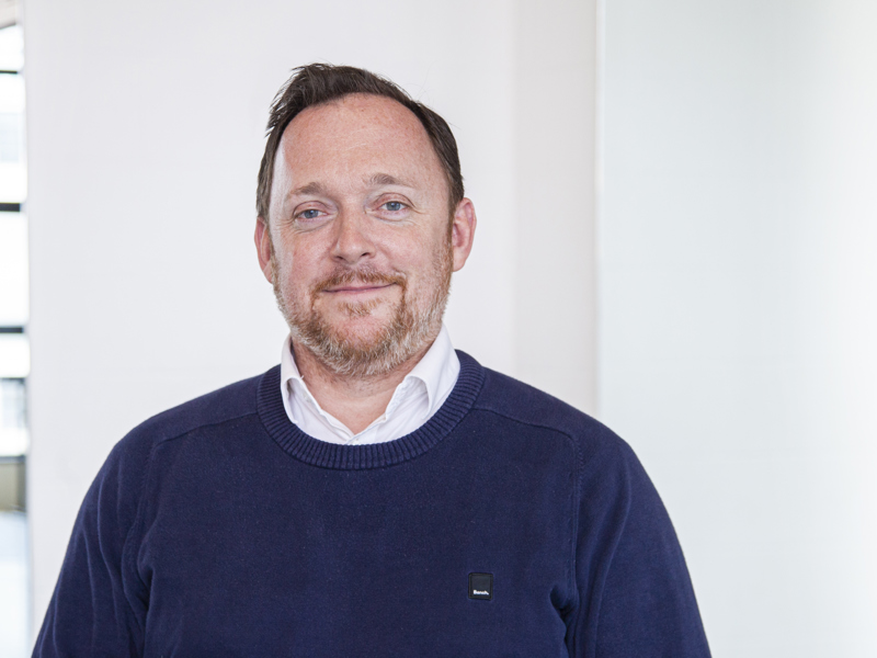 Headshot of Andrew Hurst. White male with light hair and beard smiling at camera, wearing blue jumper Headshot of Andrew Hurst. White male with light hair and beard smiling at camera, wearing blue jumper