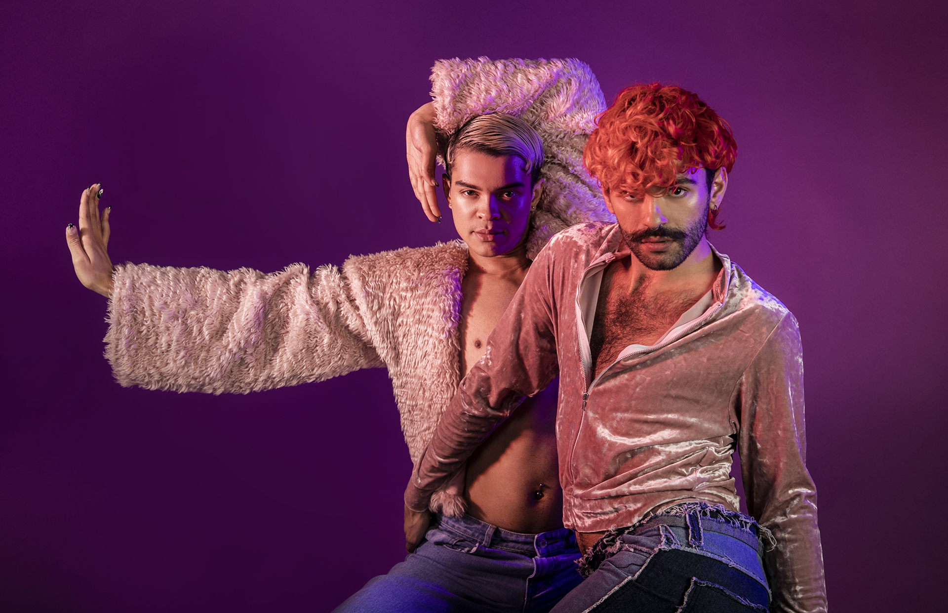 Two global majority LGBTQ+ male voguing dancers. Wearing pink tops and blue jeans on purple studio background. 
