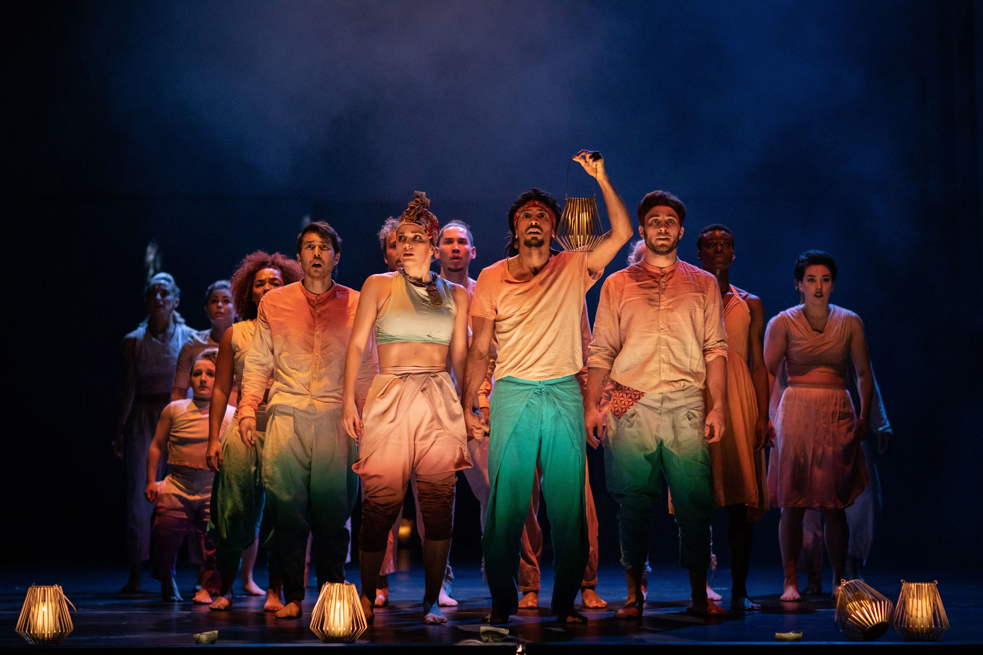 group of dancers on stage for Message in a bottle wearing colourful casual clothes looking out to the audience with one person lifting hand and clicking group of dancers on stage for Message in a bottle wearing colourful casual clothes looking out to the audience with one person lifting hand and clicking