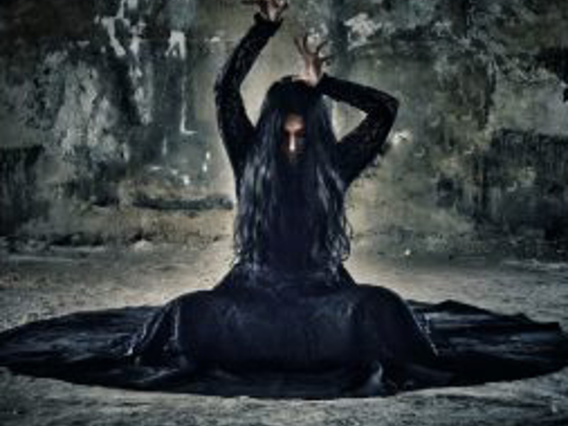 Female wearing all black with hands above head with crossed legs in a gothic room Female wearing all black with hands above head with crossed legs in a gothic room