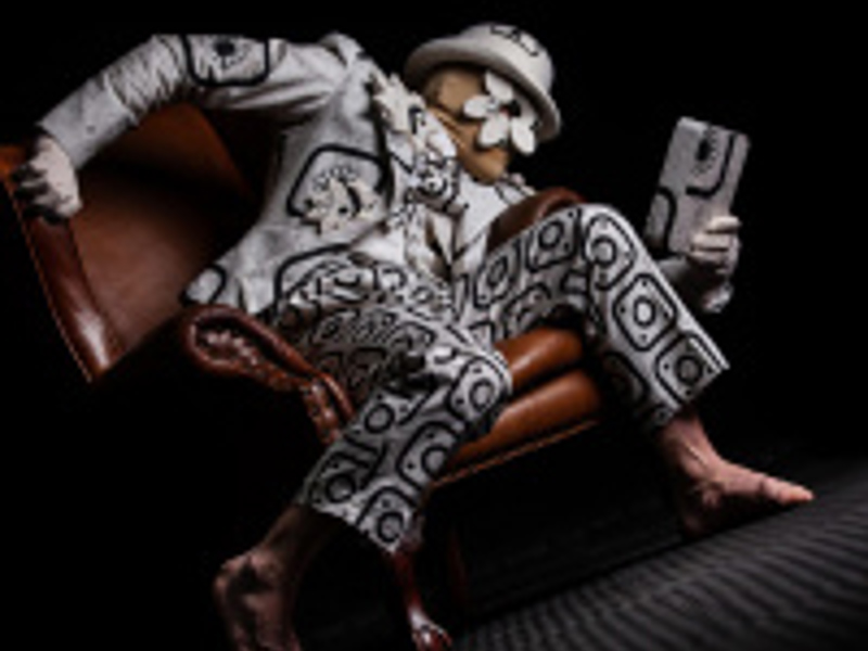 White man sitting on a chair wearing a black and white patterned suit holding a tabletwith a white top hat and white mask. White man sitting on a chair wearing a black and white patterned suit holding a tabletwith a white top hat and white mask.