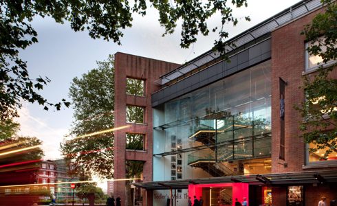 Image of the new Sadlers Wells Theatre. Large brick building with large windows with lit up red door