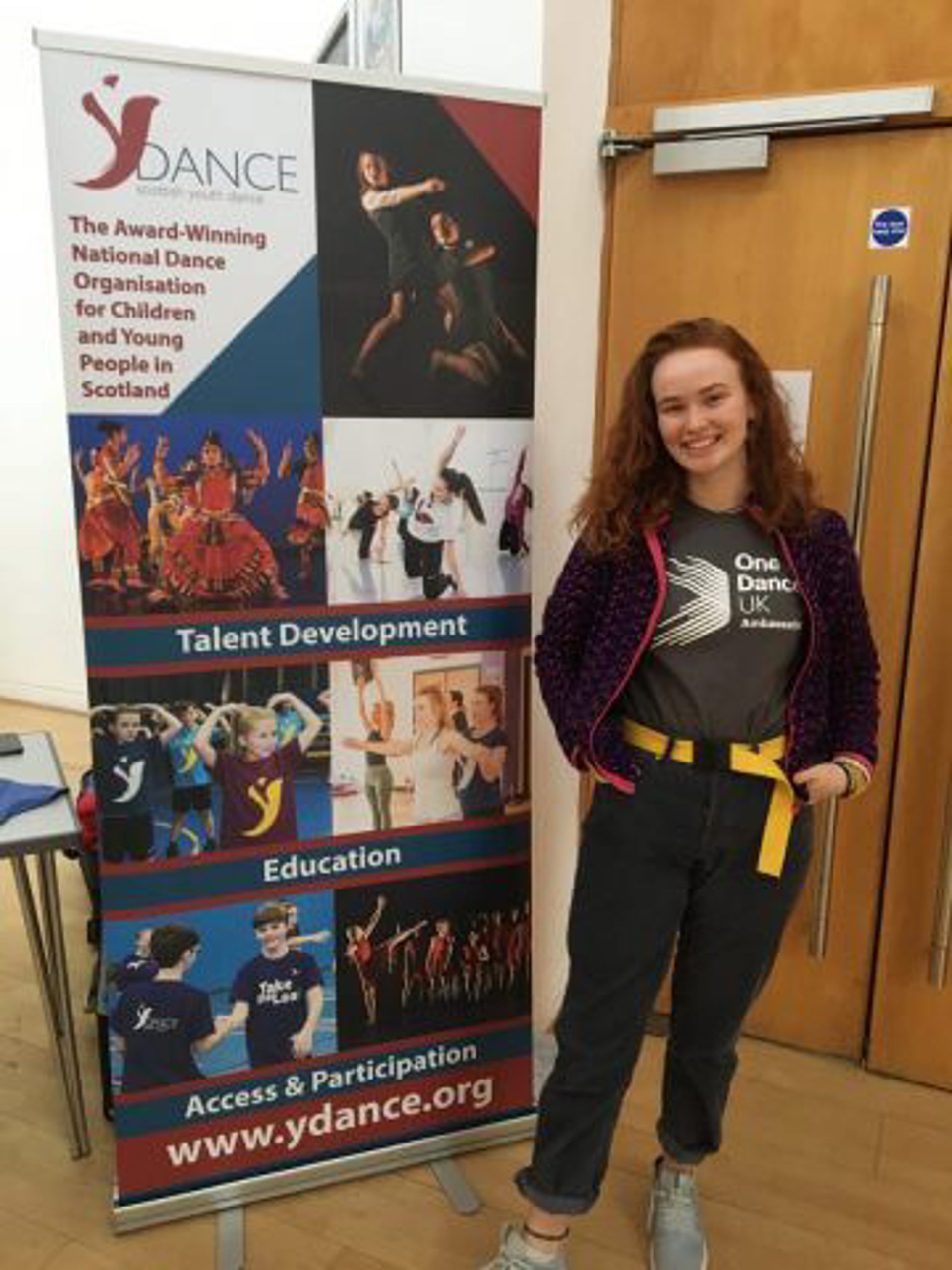 White female one dance uk dance ambassador standing in front of a Y Dance pull up banner White female one dance uk dance ambassador standing in front of a Y Dance pull up banner