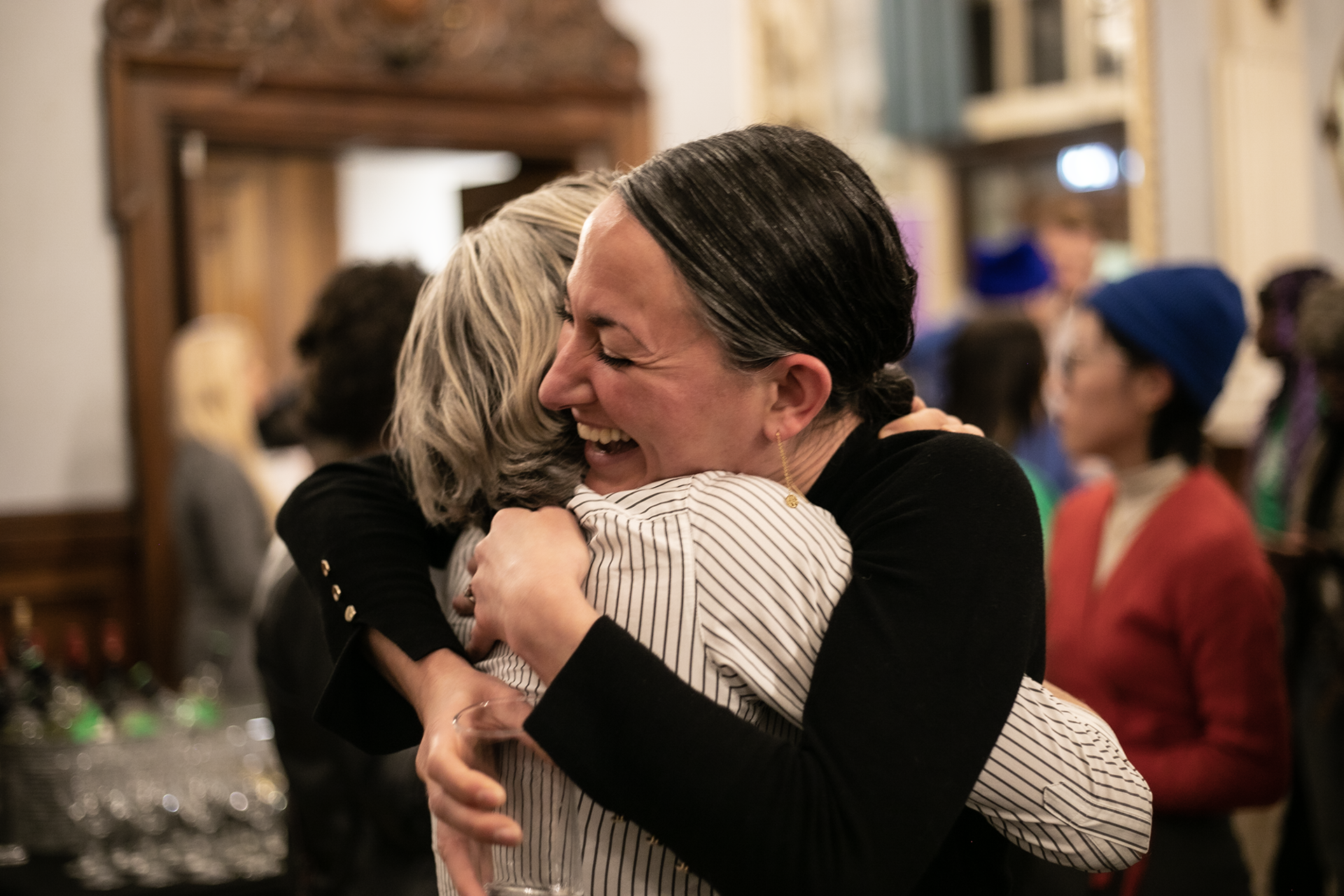 Two females hugging with big smiles with a crowded room Two females hugging with big smiles with a crowded room