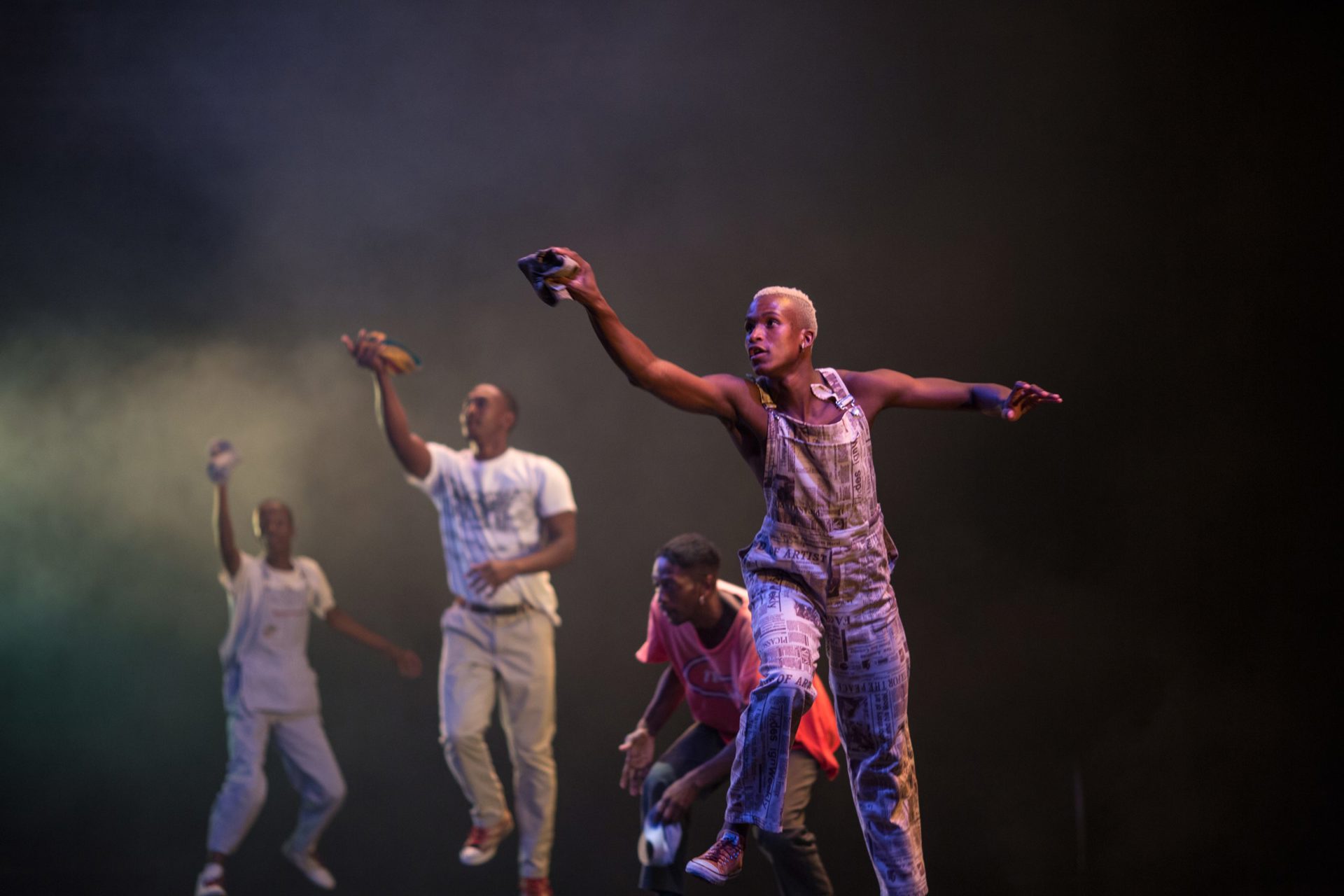 four male global majority dancers on dark stage with one arm in the air holding a cloth. four male global majority dancers on dark stage with one arm in the air holding a cloth.