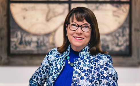 white female with brown hair and rectangle glasses. Wearing blue floral blazer and blue top