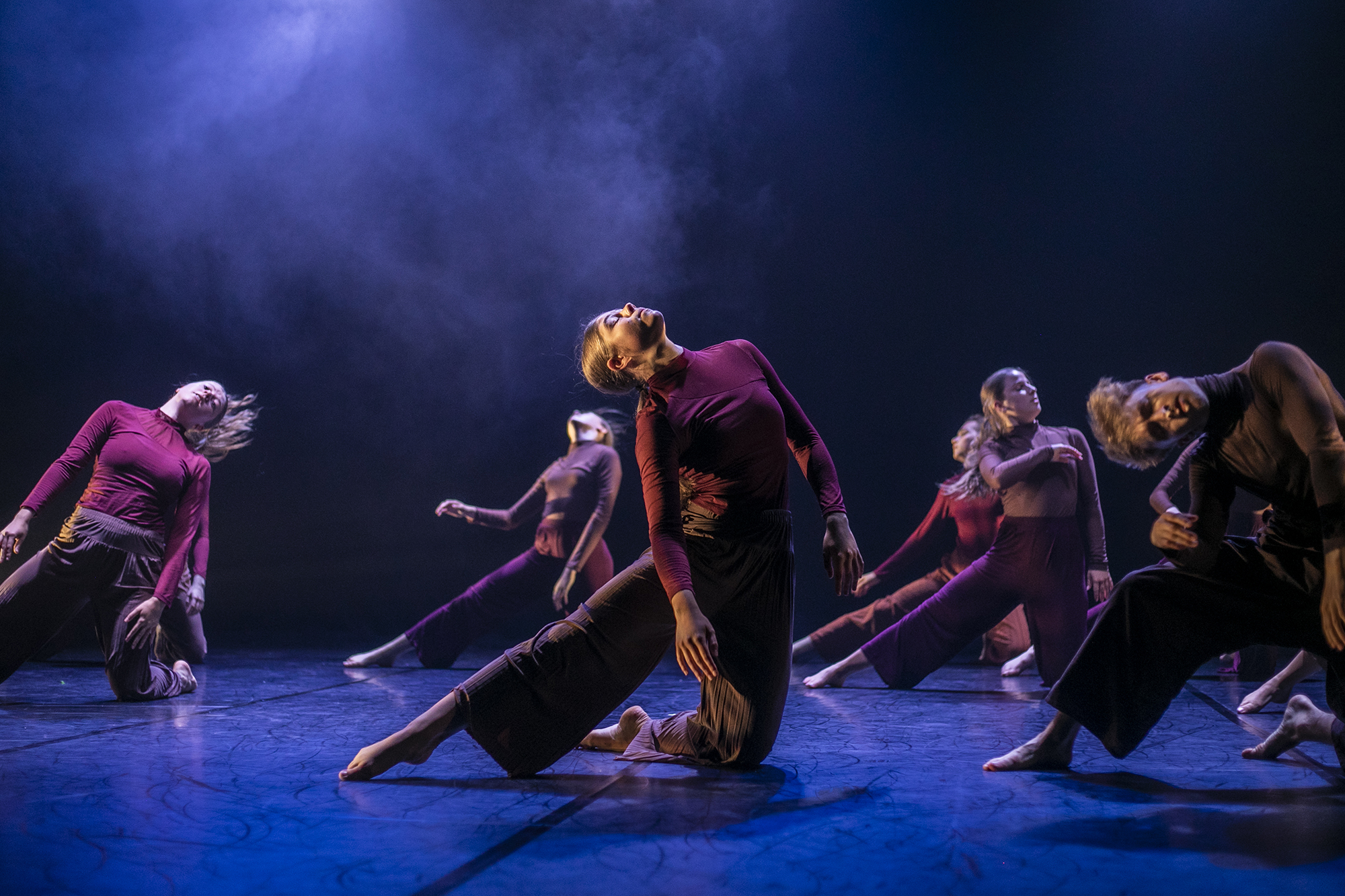6 female dancers performing on the U.Dance stage wearing long sleve red tops and baggy brown trousers. All staners on one know with the other leg straight to the left with heads titled to the sky. Stage lighting is dark with blue fog and floor. 6 female dancers performing on the U.Dance stage wearing long sleve red tops and baggy brown trousers. All staners on one know with the other leg straight to the left with heads titled to the sky. Stage lighting is dark with blue fog and floor.