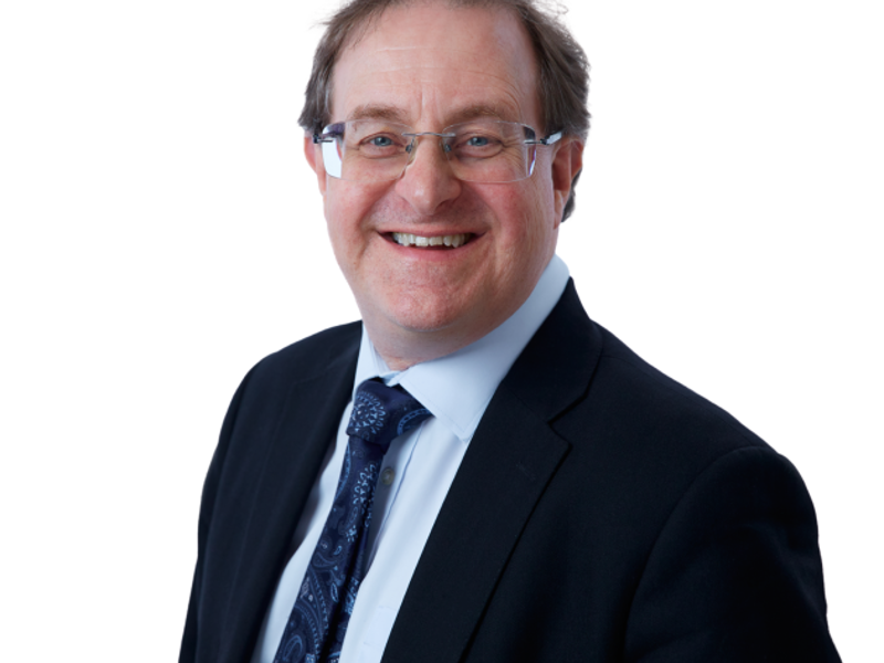 Headshot of Julian Flitter. White male with short dark hair. Wearing glasses, dark blue suit, light blue shirt and blue tie.