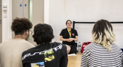 One Dance UK staff member sitting on knees talking to three students sitting in front of the camera in a dance studio. 