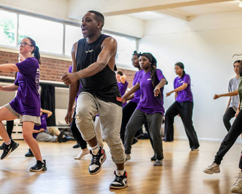 black male dancer  teaching a group of young people to dance. all in a running man position wearing athletic clothing in a dance studio. 