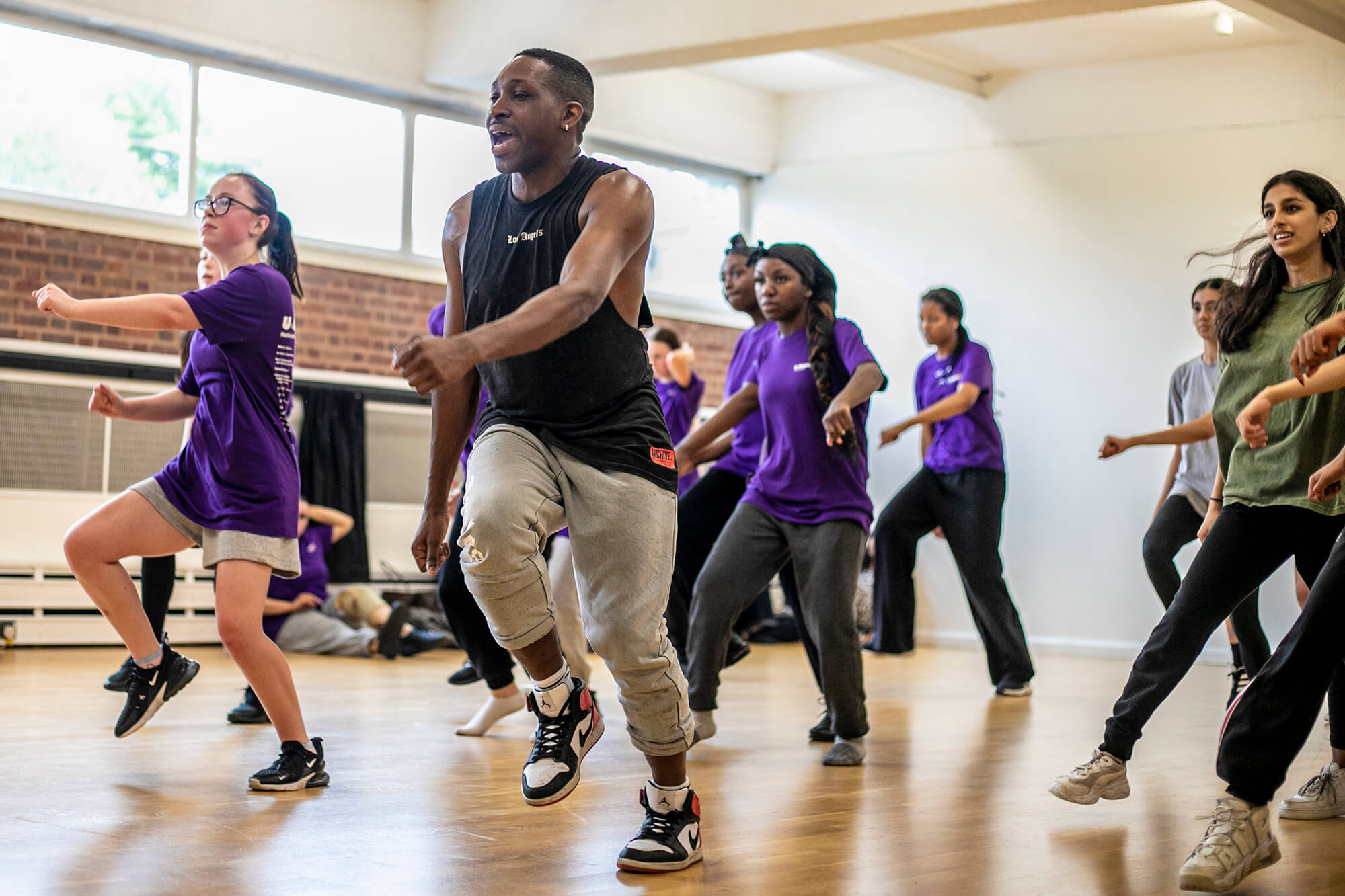black male dancer  teaching a group of young people to dance. all in a running man position wearing athletic clothing in a dance studio. 