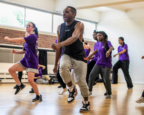 black male dancer  teaching a group of young people to dance. all in a running man position wearing athletic clothing in a dance studio. 