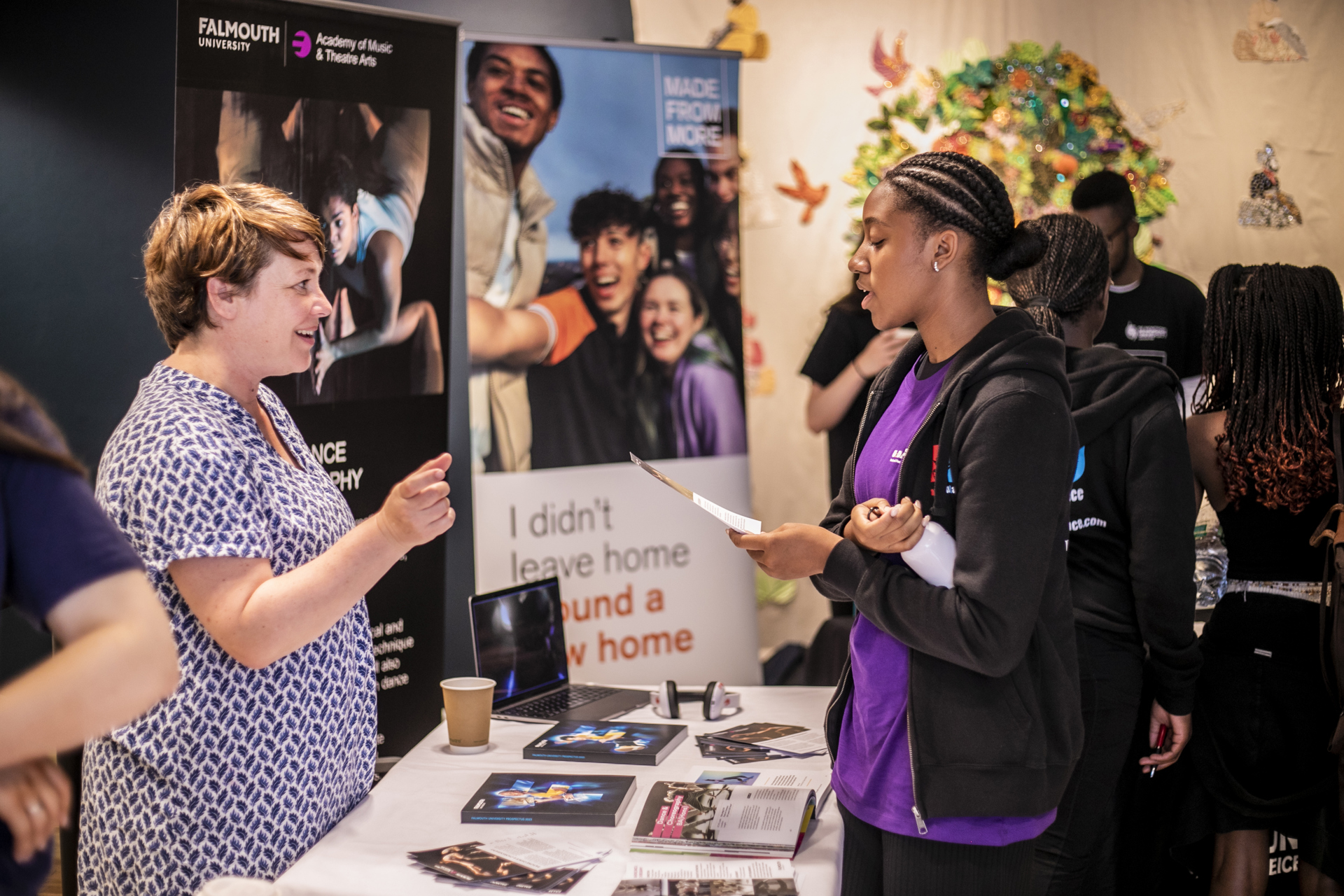 female standing at an exhibition stand talking to a young female who is holding a leaflet. Behind them are pull up banners female standing at an exhibition stand talking to a young female who is holding a leaflet. Behind them are pull up banners