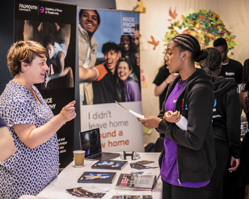 female standing at an exhibition stand talking to a young female who is holding a leaflet. Behind them are pull up banners 