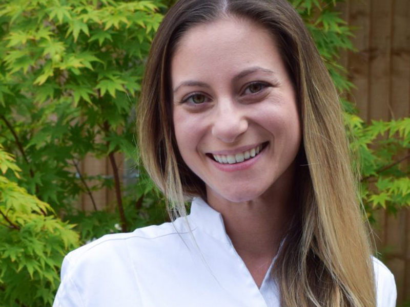 Headshot of Nonica Papageorgiou. White female with long blonde hair smiling at the camera wearing white shirt.