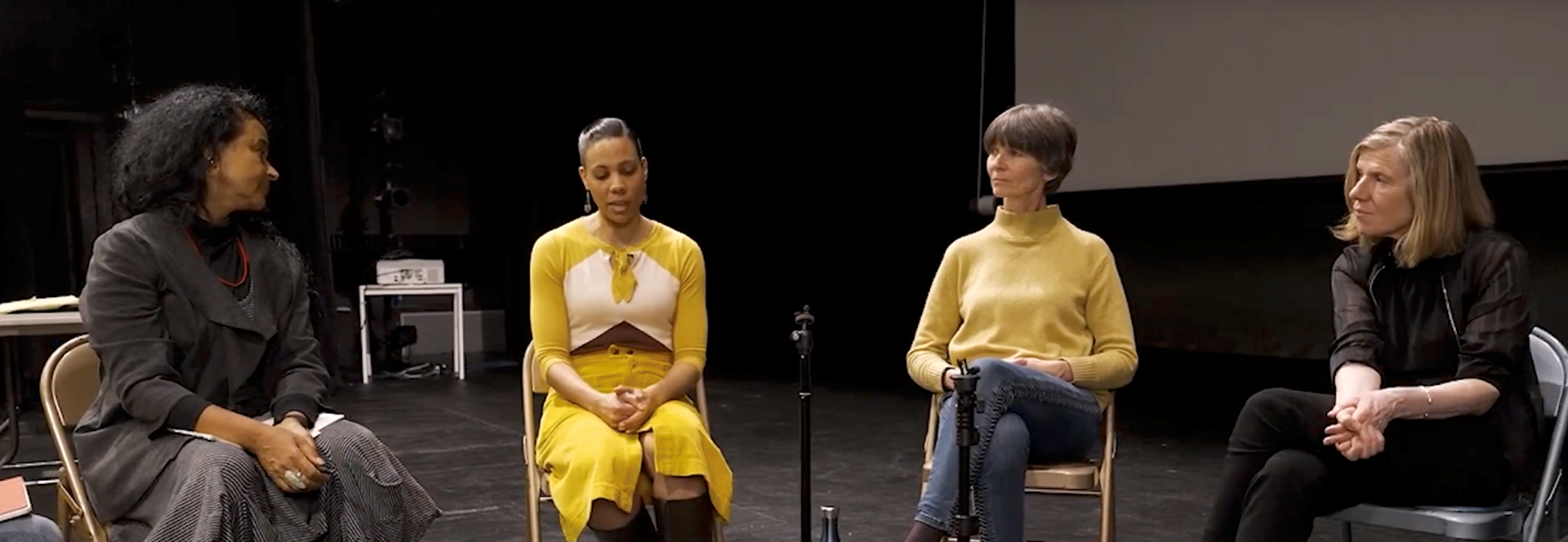 Four females sitting on stage with a microphone on a disscussion panel Four females sitting on stage with a microphone on a disscussion panel