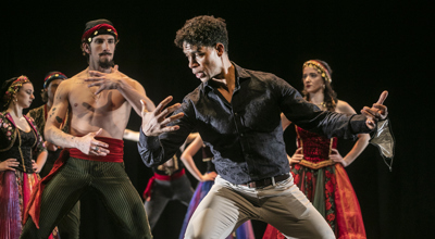 Male cuban dancer Carlos Acosta leaning to the left pretending to hold someone showing male dancer how to perform the move. All in colourful traditional cuban costumes