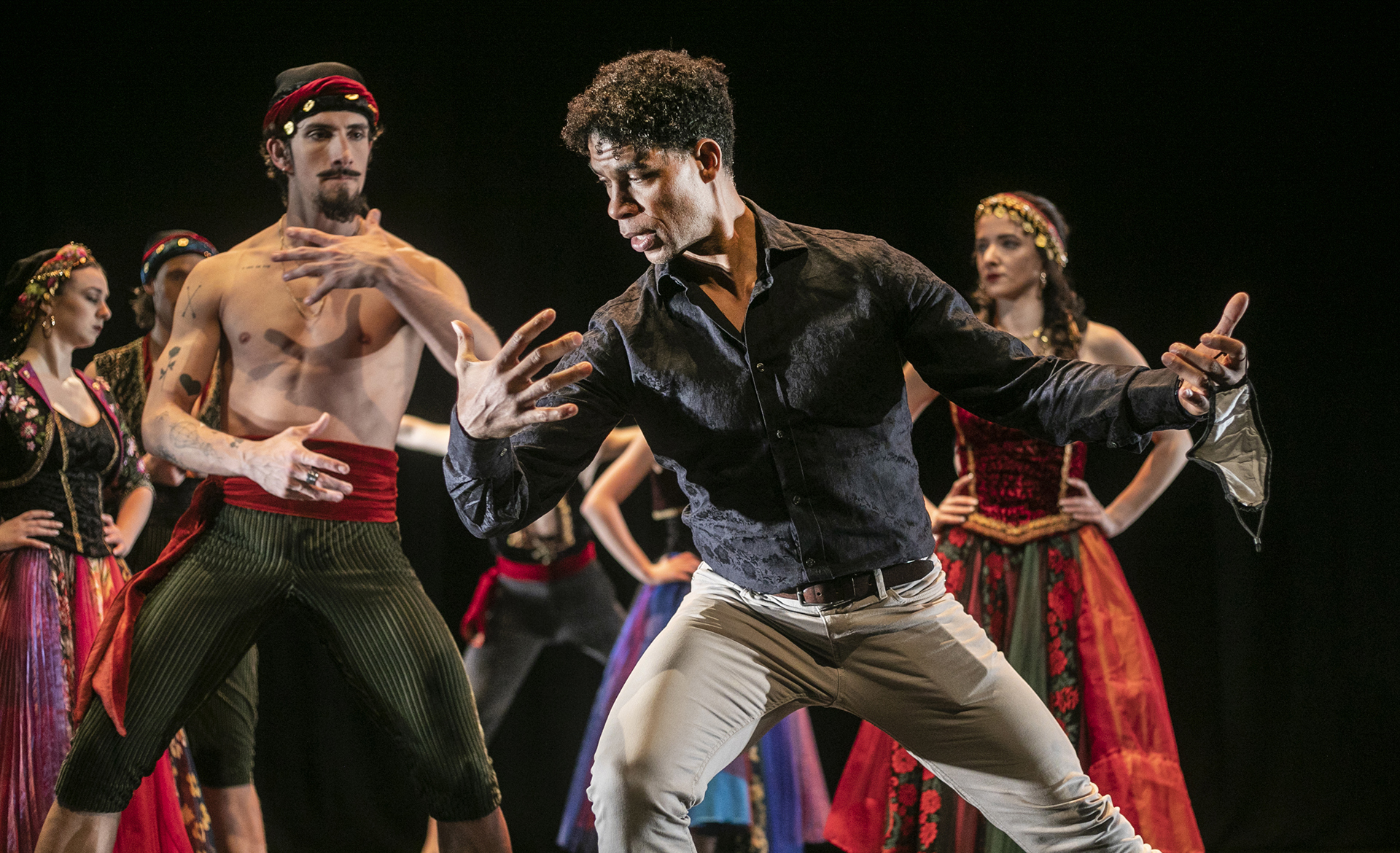 Male cuban dancer Carlos Acosta leaning to the left pretending to hold someone showing male dancer how to perform the move. All in colourful traditional cuban costumes