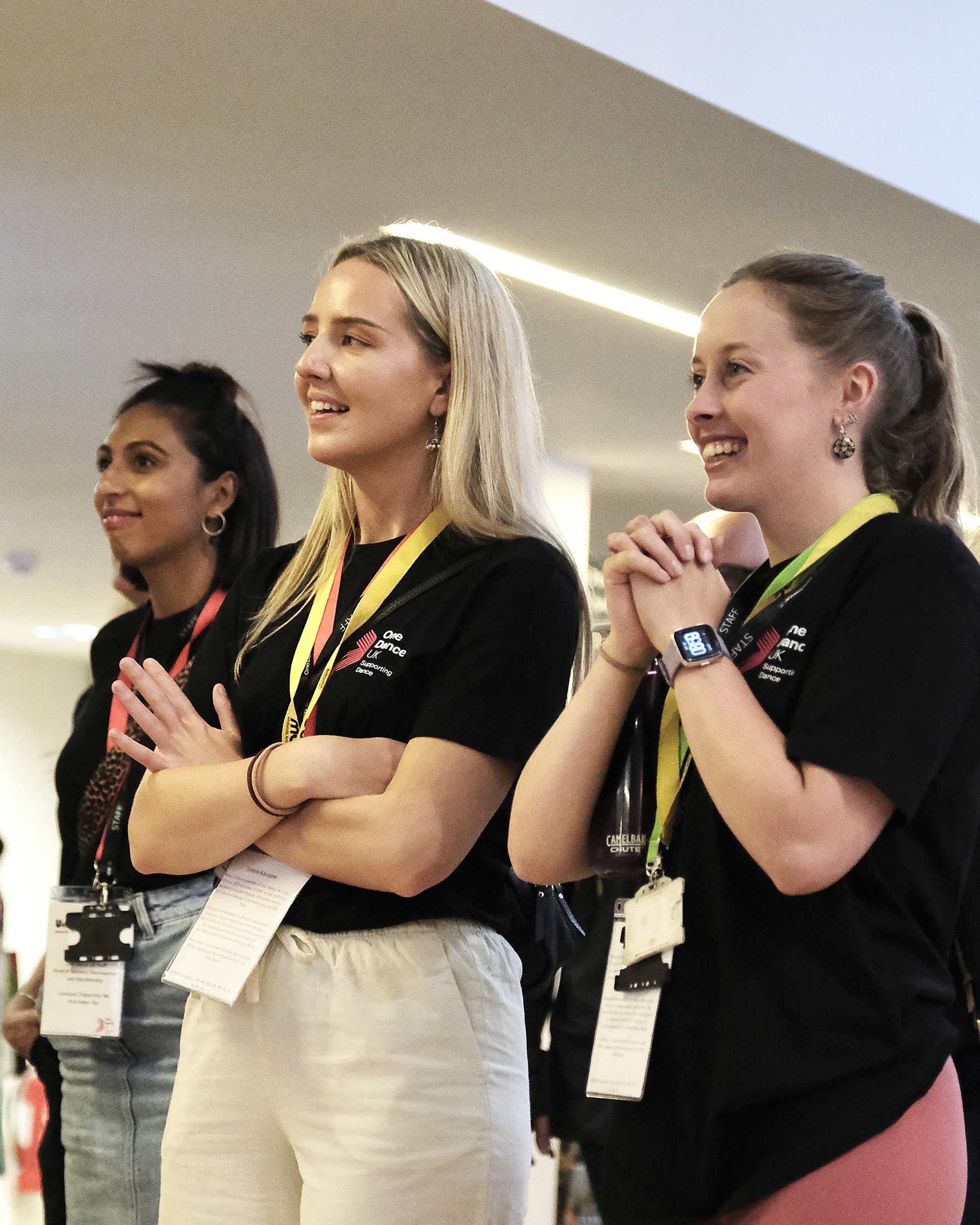 Three female One Dance UK staff members smiling in a foyer whilst watching a performance 