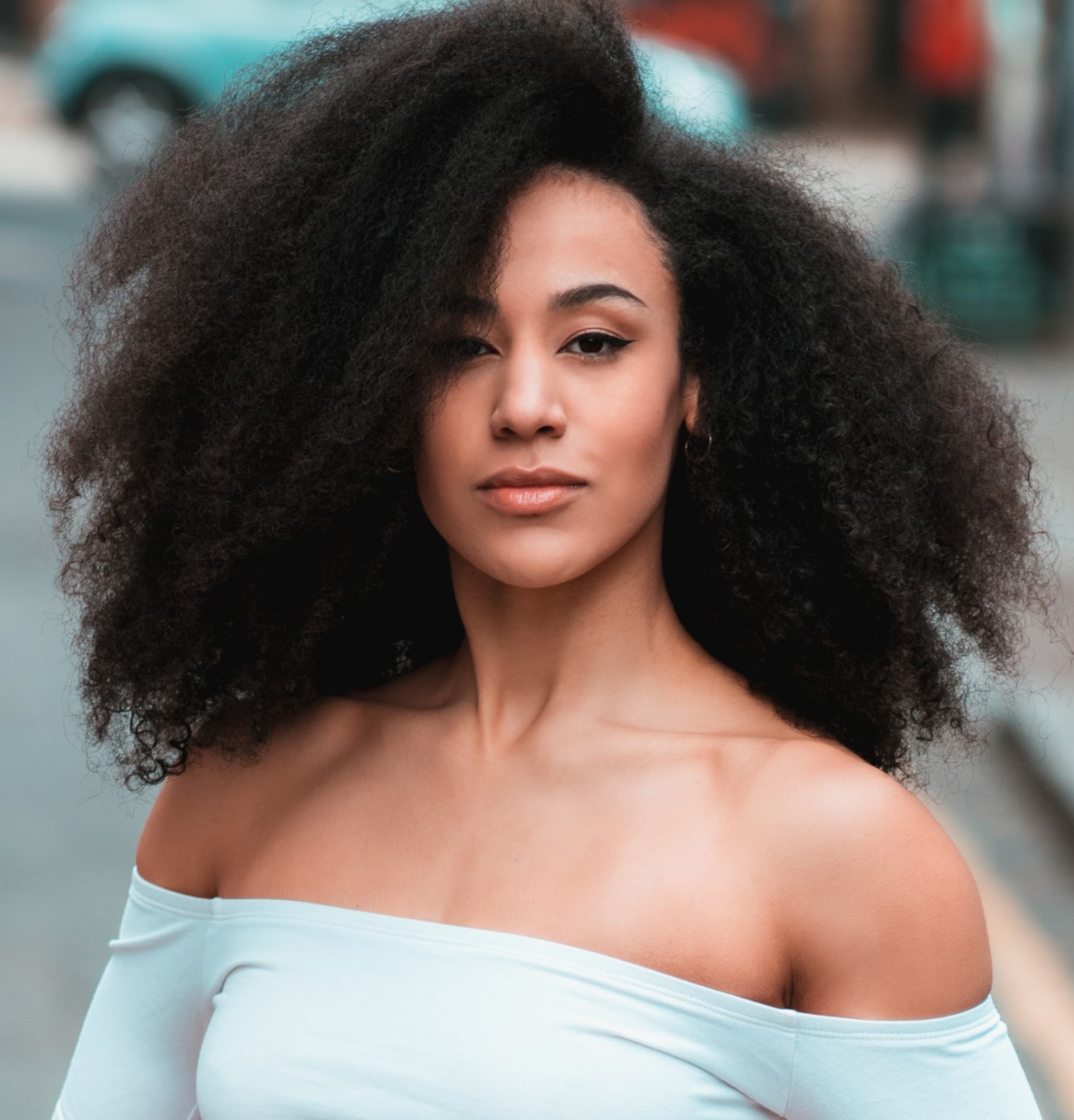 head shot of Jessica Walker. Global majority female with big afro looking at camera wearing an off the shoulder blue top