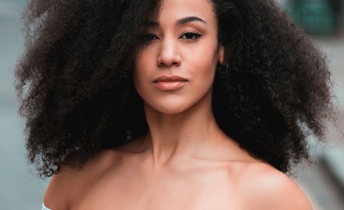head shot of Jessica Walker. Global majority female with big afro looking at camera wearing an off the shoulder blue top