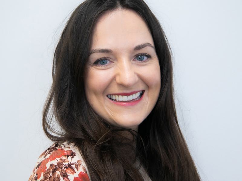 Headshot of Colette Stanton. White female with long brown hair smiling at the camera wearing red flowery top.