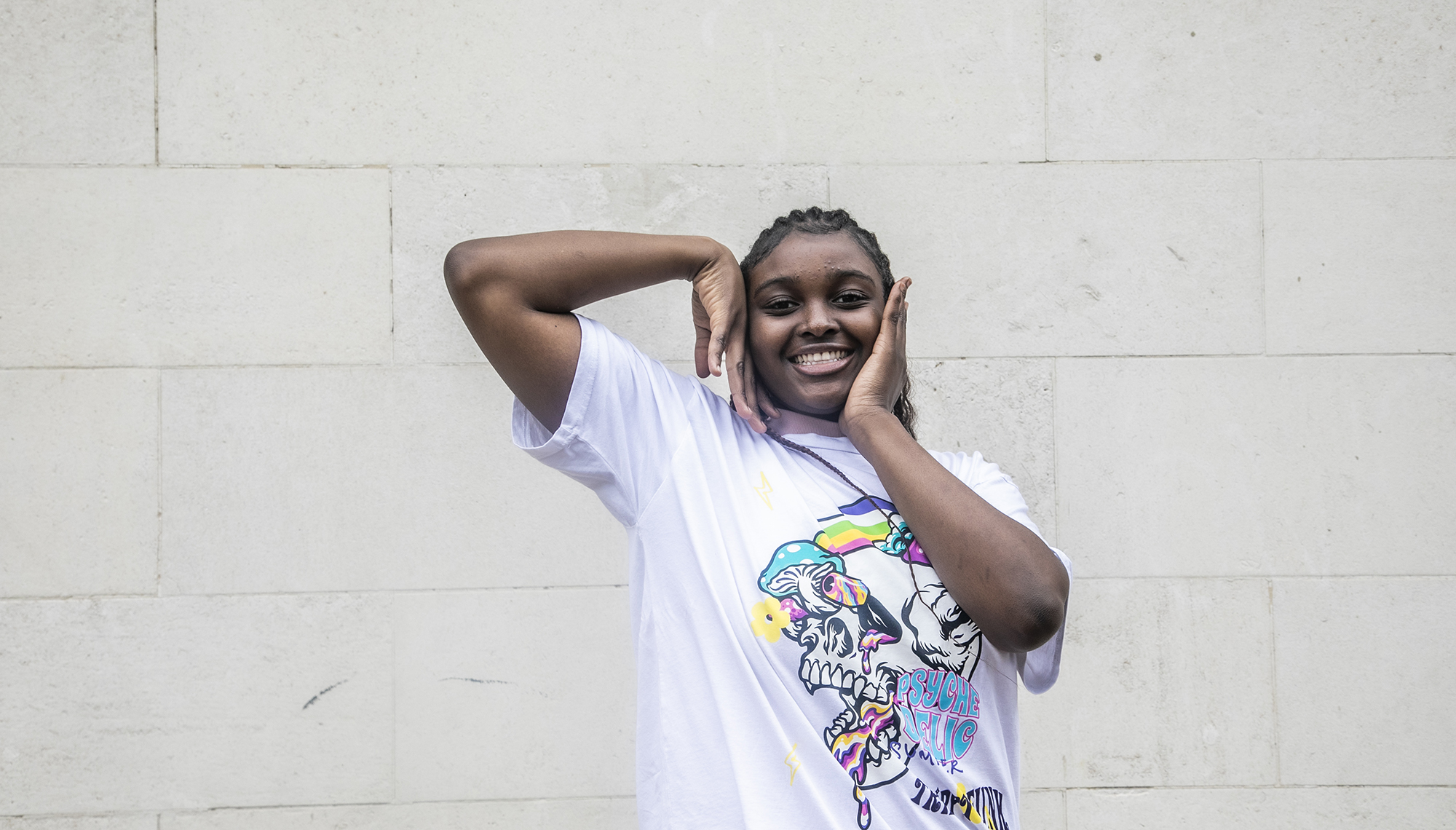 young global majority female dancer with long black braids. Arms framing the face. Wearing white graphic tshirt young global majority female dancer with long black braids. Arms framing the face. Wearing white graphic tshirt