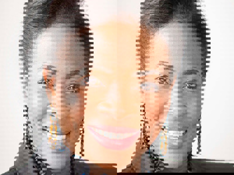 Headshot of Denise Nurse. Global majority female with tied back dark hair, smiling. Wearing large hoop earrings, black blazer and ruffled black top. Headshot of Denise Nurse. Global majority female with tied back dark hair, smiling. Wearing large hoop earrings, black blazer and ruffled black top.