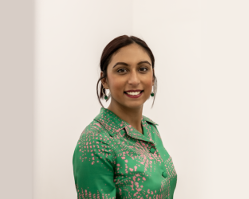 Headshot of Alisha Kadri. Global majority female with brown hair tied back wearing green button up top smiling