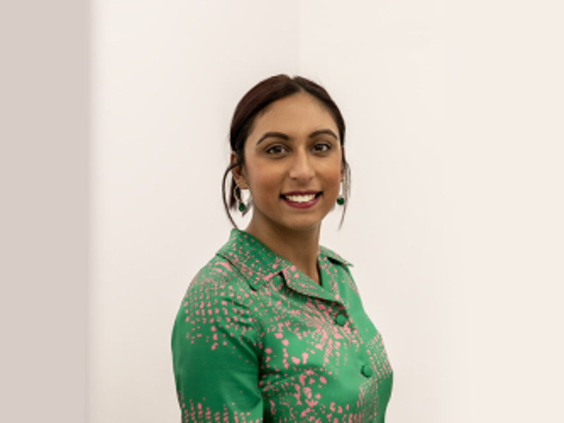 Headshot of Alisha Kadri. Global majority female with brown hair tied back wearing green button up top smiling