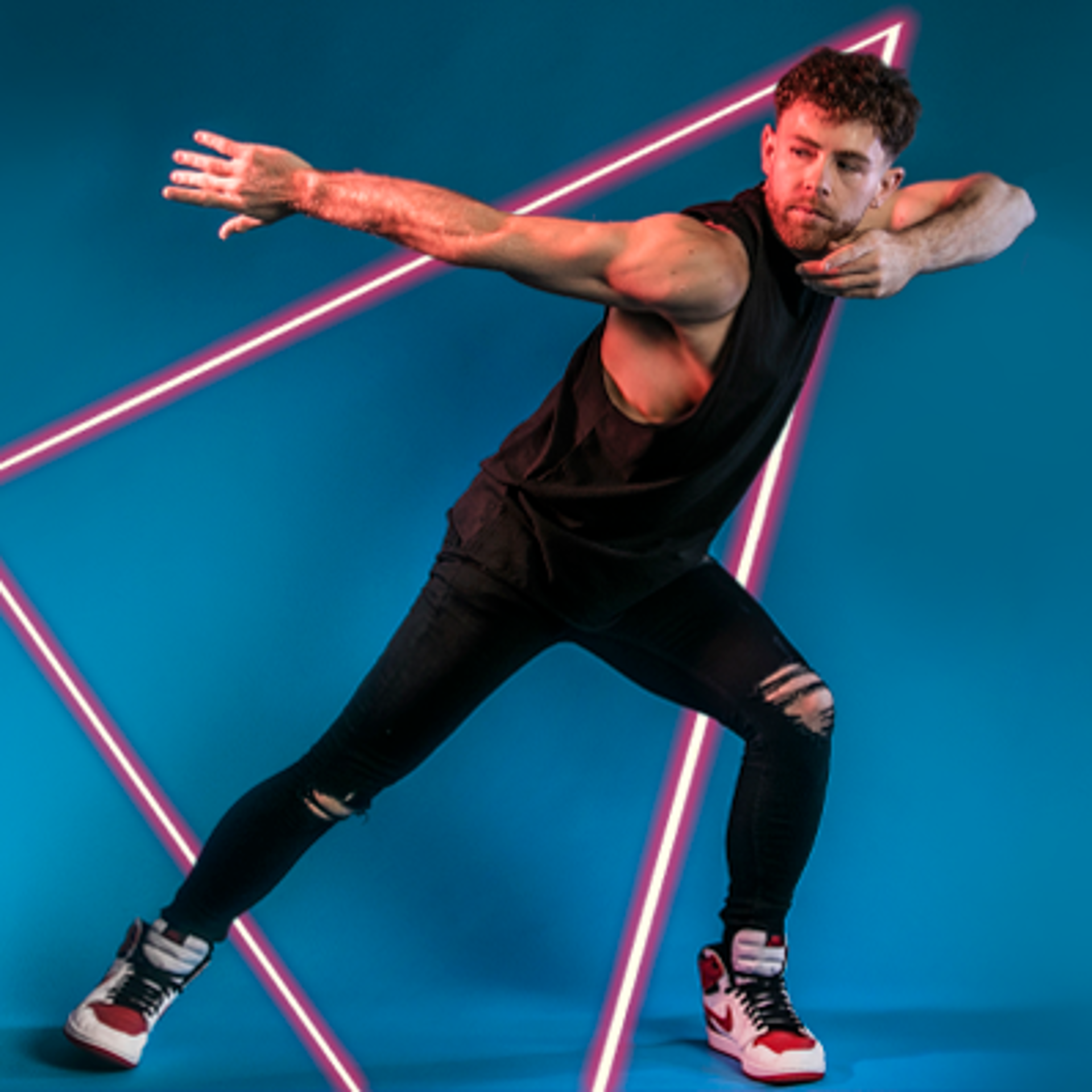 white male dancer lunging to the right with arms pointed to the left. Black outfit and white trainers. On blue studio background. 
