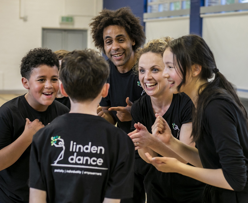 teachers and dance students excitedly talking together in black PE kit with sports hall