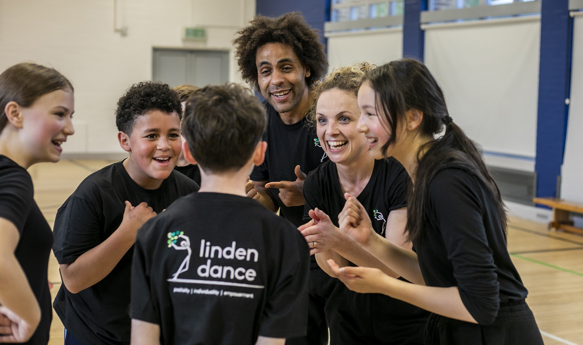 teachers and dance students excitedly talking together in black PE kit with sports hall teachers and dance students excitedly talking together in black PE kit with sports hall