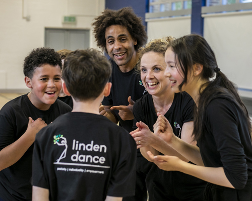 teachers and dance students excitedly talking together in black PE kit with sports hall