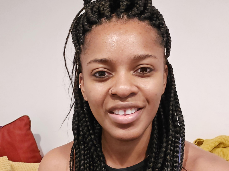 Headshot of Genevieve Tawiah. Global majority female with long dark braided hair smiling at the camera. Wearing black sports top