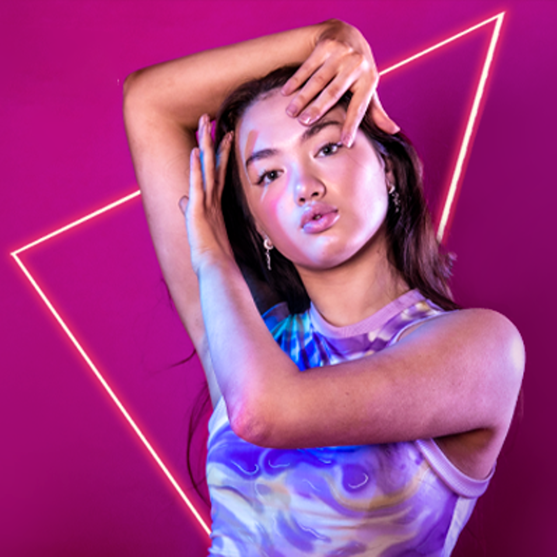 global majority dancer with hands infront and around face on hot pink studio background. Wearing marbled purple crop top.