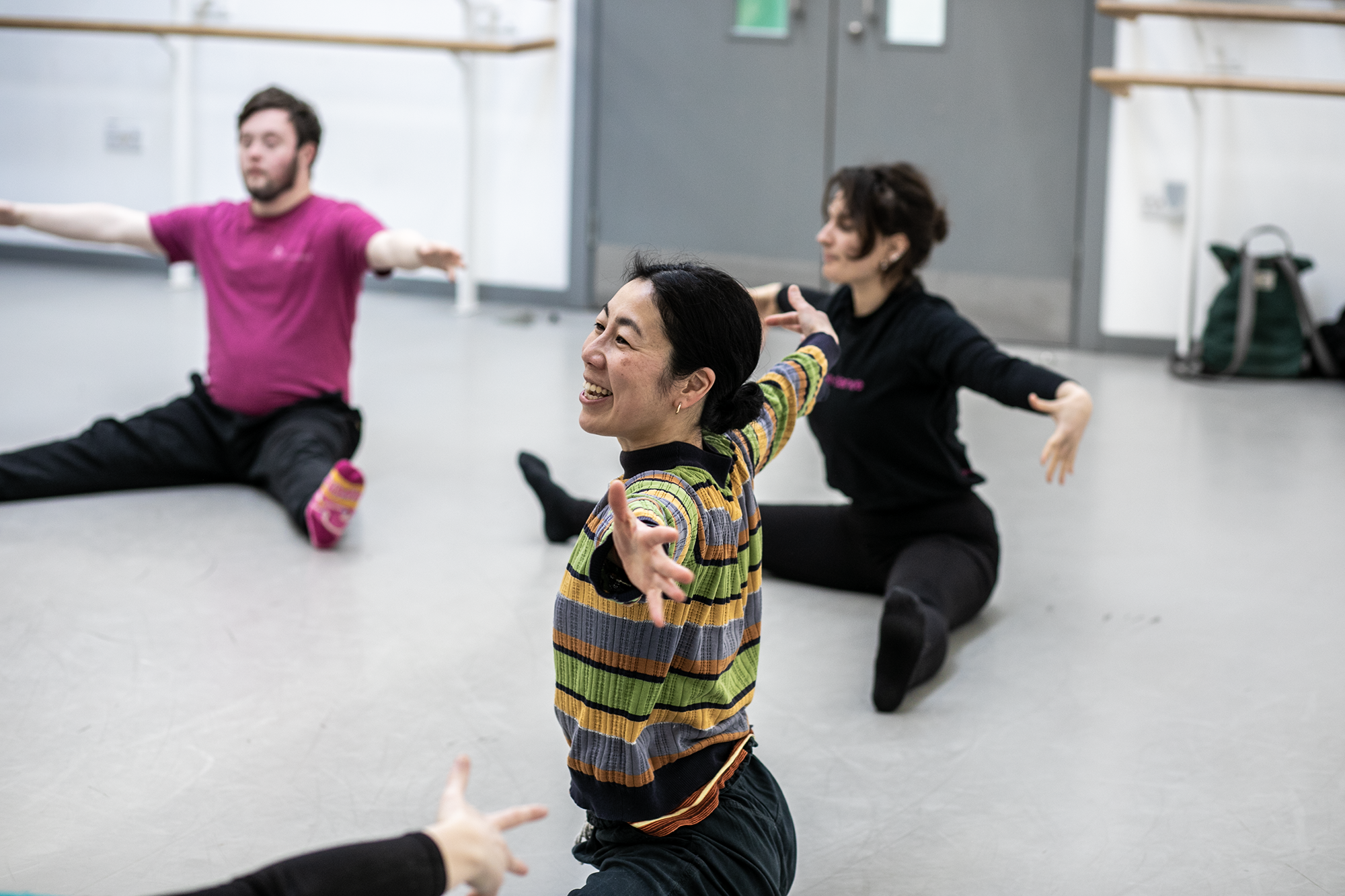 global majority female dancer teaching community group. Arm stretched open sitting with legs wise on the floor in the dance studio.  global majority female dancer teaching community group. Arm stretched open sitting with legs wise on the floor in the dance studio.