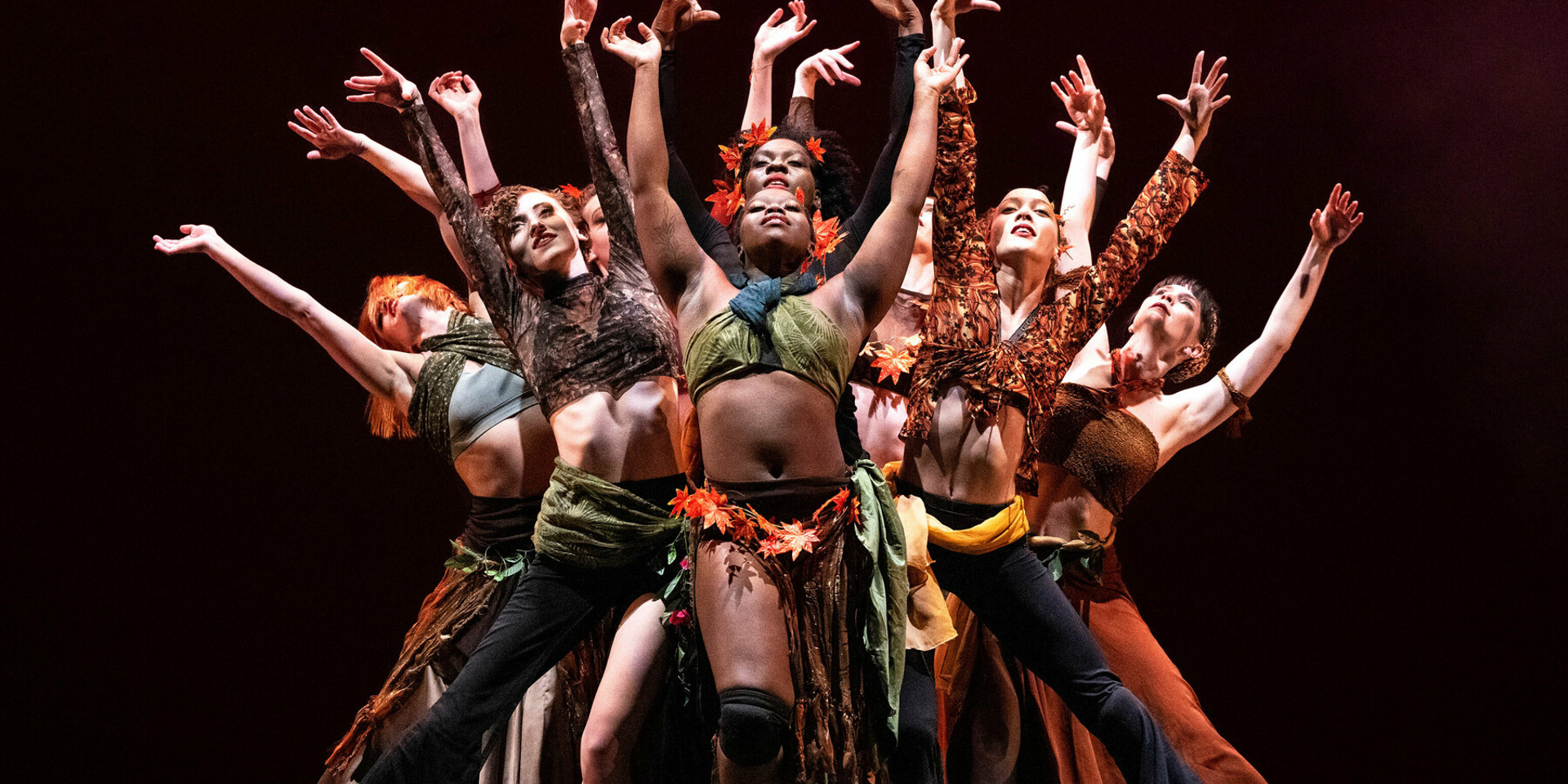 group of dancers with their arms fanned over their head on dark stage