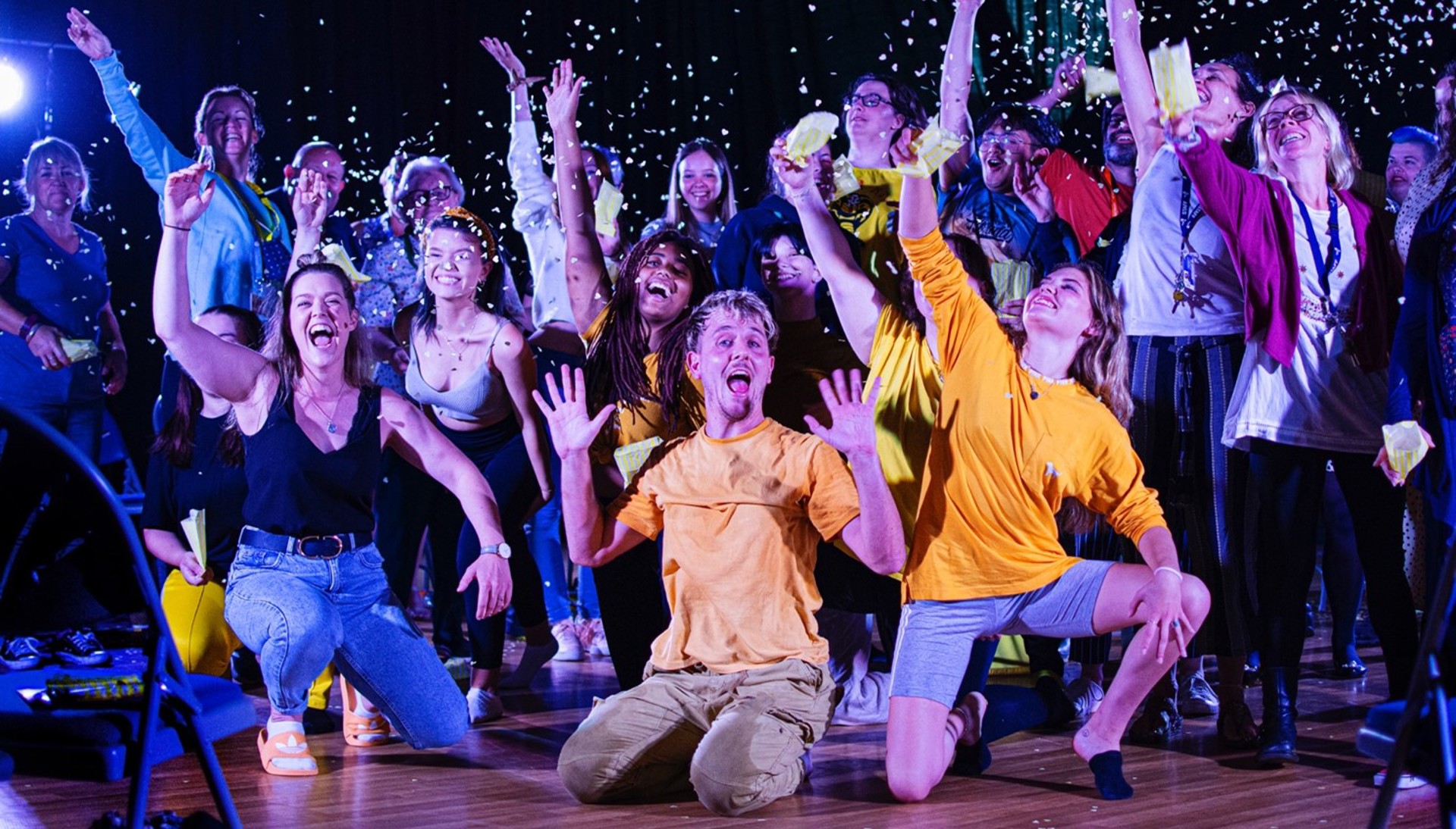 group of people wearing colour clothes on stage waving arms in the air with confetti in the air group of people wearing colour clothes on stage waving arms in the air with confetti in the air