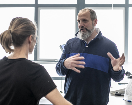 White male physiologist explaining something to white female dancer. In a white laboratory setting with a window in the background