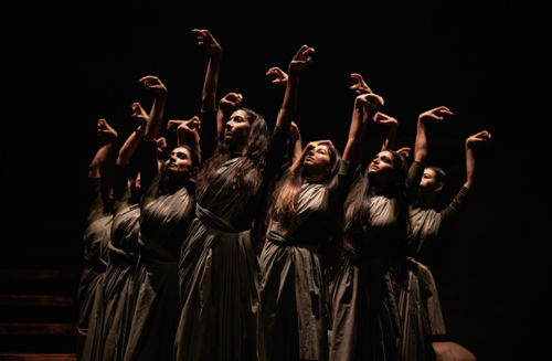 Dancers on stage with arms lifted, looking off to the left