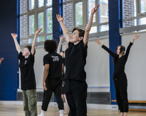 primary school boys and girls all reaching up to the sky in a sports hall