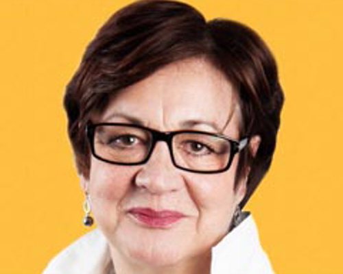 Headshot of Susannah Simons. White female with short dark hair. Wearing rectangular glasses and a white shirt on a yeallow background