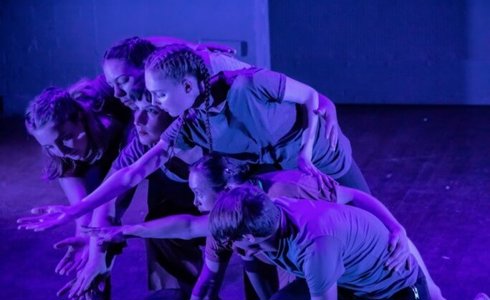six young dancers all huddled together reaching for the same spot in the bottom left on the screen with blue lighting