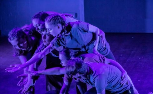 six young dancers all huddled together reaching for the same spot in the bottom left on the screen with blue lighting
