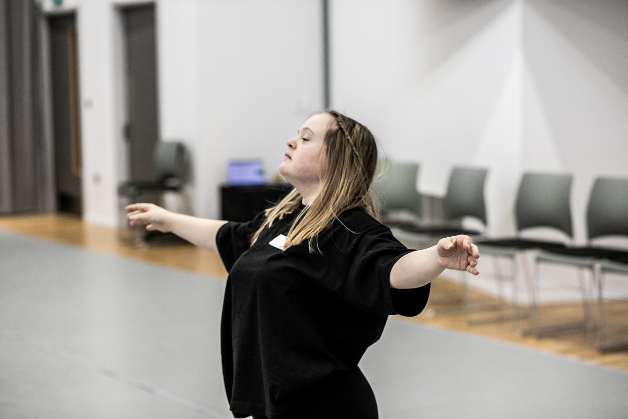 White blonde female down syndrome dancer with arms spread out head up wearing black in a dance studio White blonde female down syndrome dancer with arms spread out head up wearing black in a dance studio
